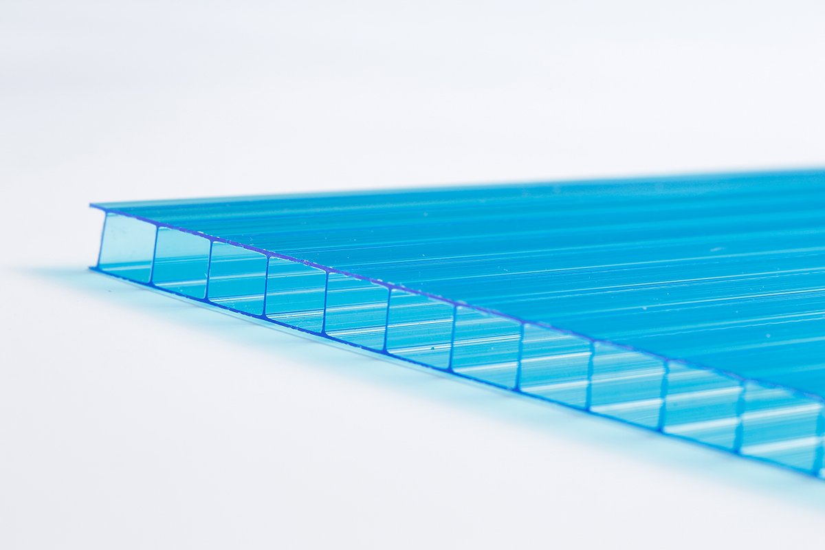 e05a577736b9d1b173b93fc885e7cbb6 - Close-up of a blue translucent corrugated plastic sheet with evenly spaced vertical ribs along the cut edge on a white surface.