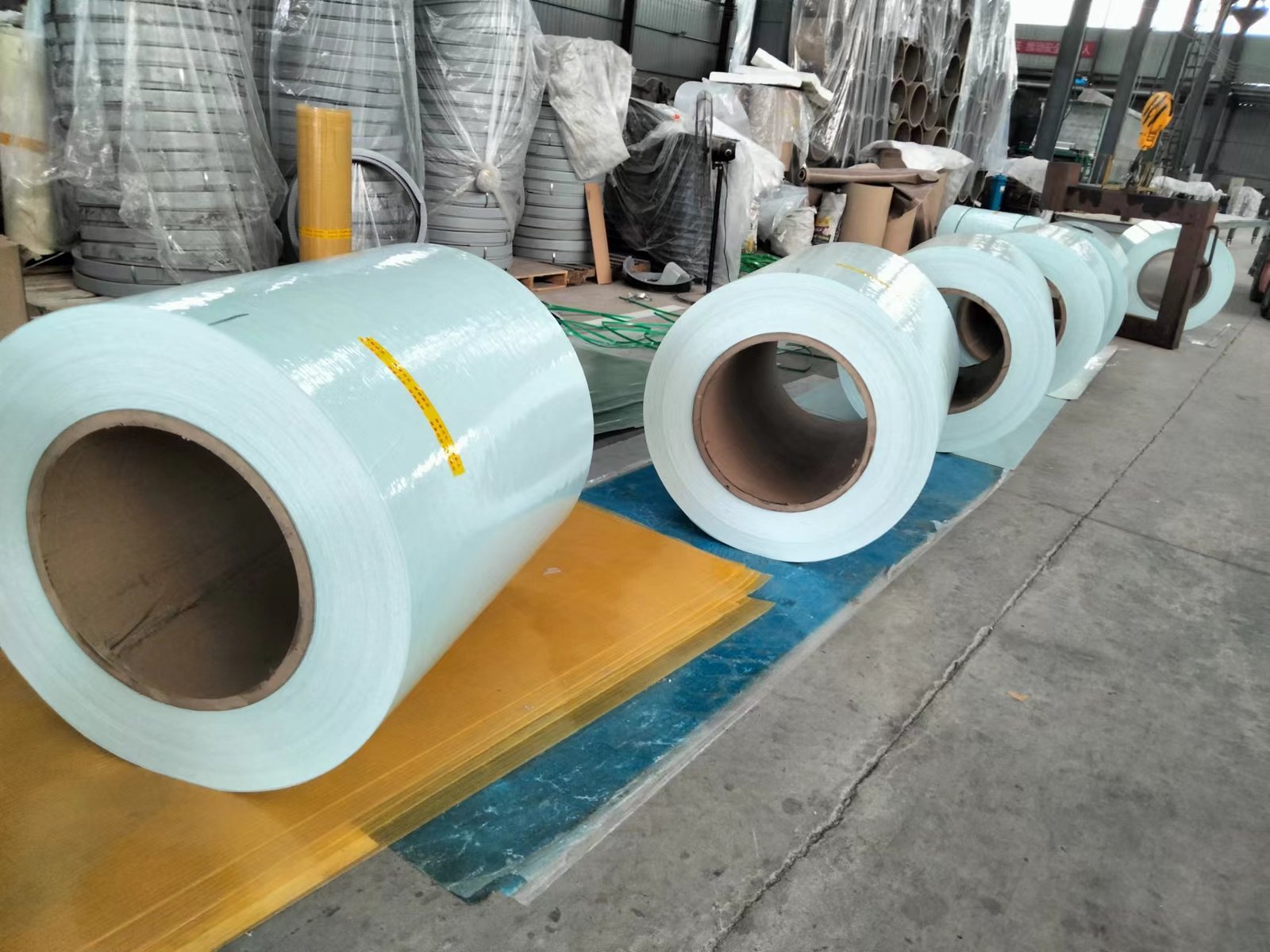 微信图片_20260216231345_138_14 - Large light-blue metal coils on the factory floor near stacked materials and equipment in a warehouse.