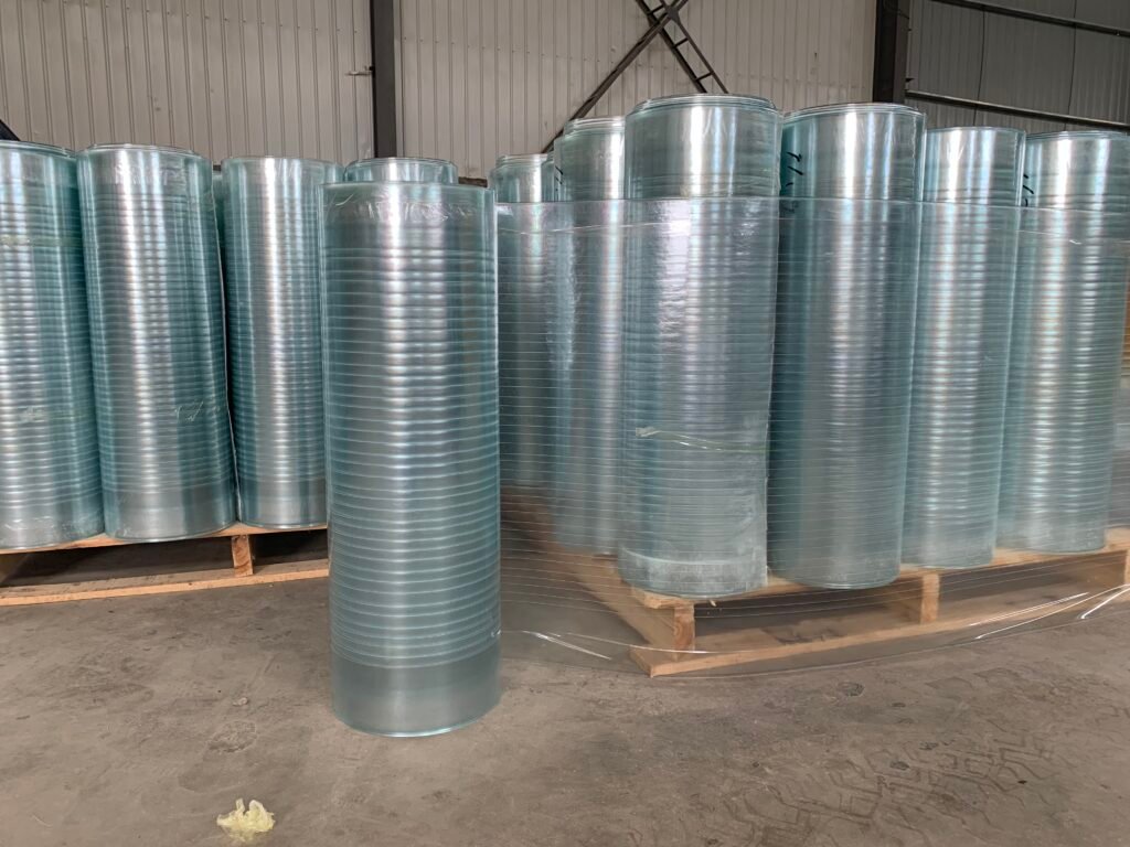 Row of shiny galvanized metal rolls standing upright in a warehouse on wooden pallets.