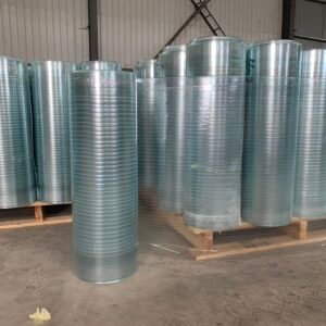 Row of shiny galvanized metal rolls standing upright in a warehouse on wooden pallets.