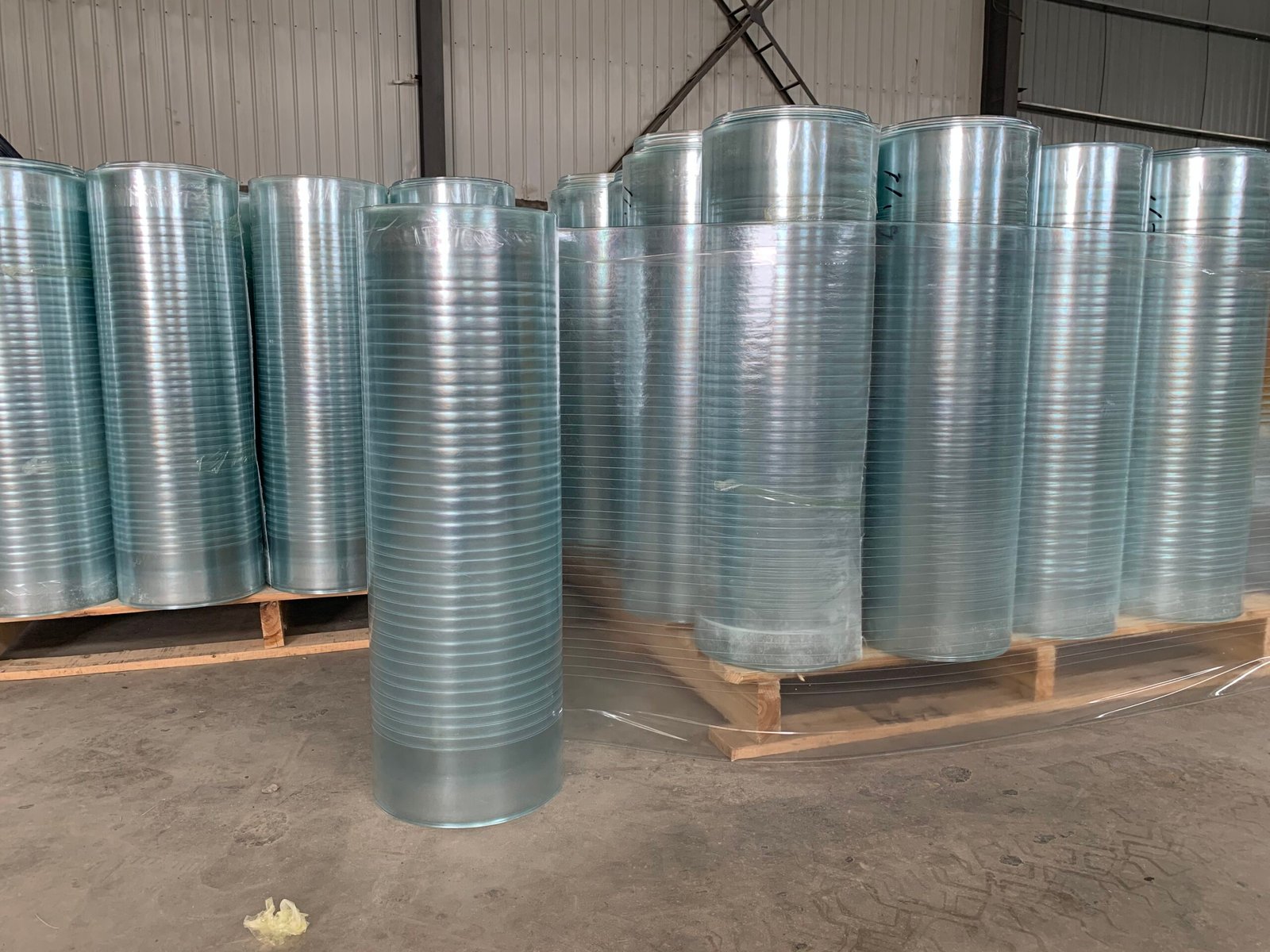微信图片_20260216231415_144_14 - Row of shiny galvanized metal rolls standing upright in a warehouse on wooden pallets.