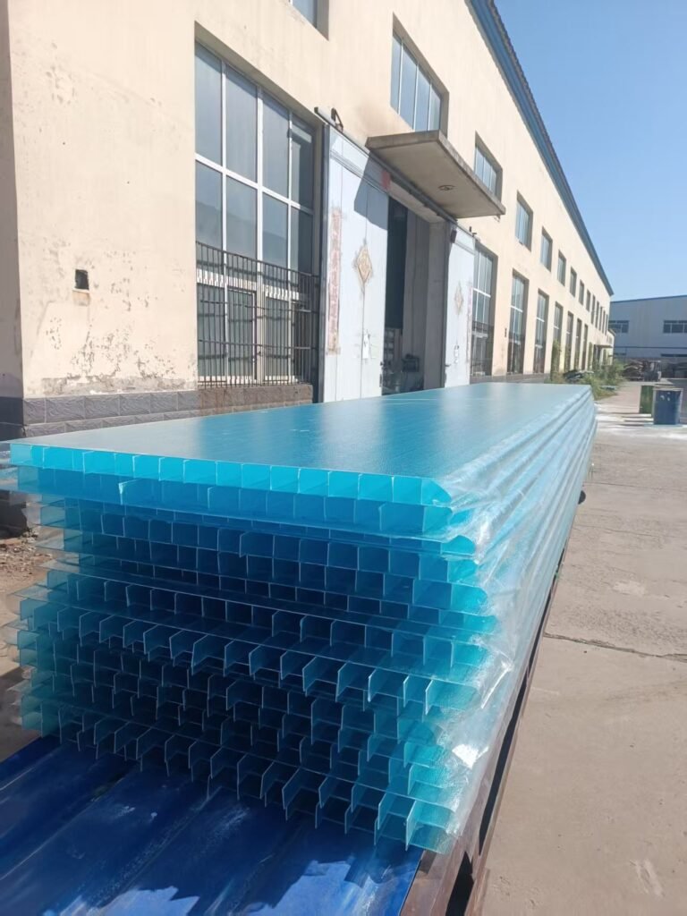 微信图片_20260221081543_7_1194 - Stack of blue-painted metal channel profiles wrapped in plastic, stacked outside a warehouse loading dock area.