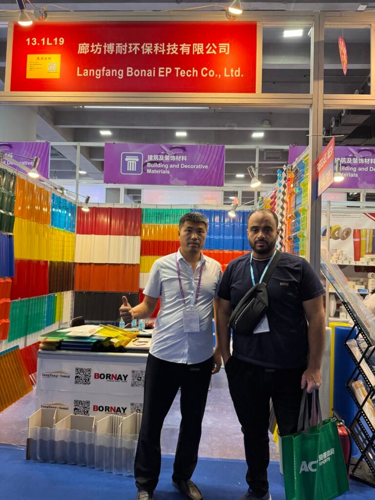 微信图片_20260330144110_441_14 - Two men stand at a trade show booth with colorful plastic panels on display; the banner above reads Langfang Bonai EP Tech Co., Ltd.