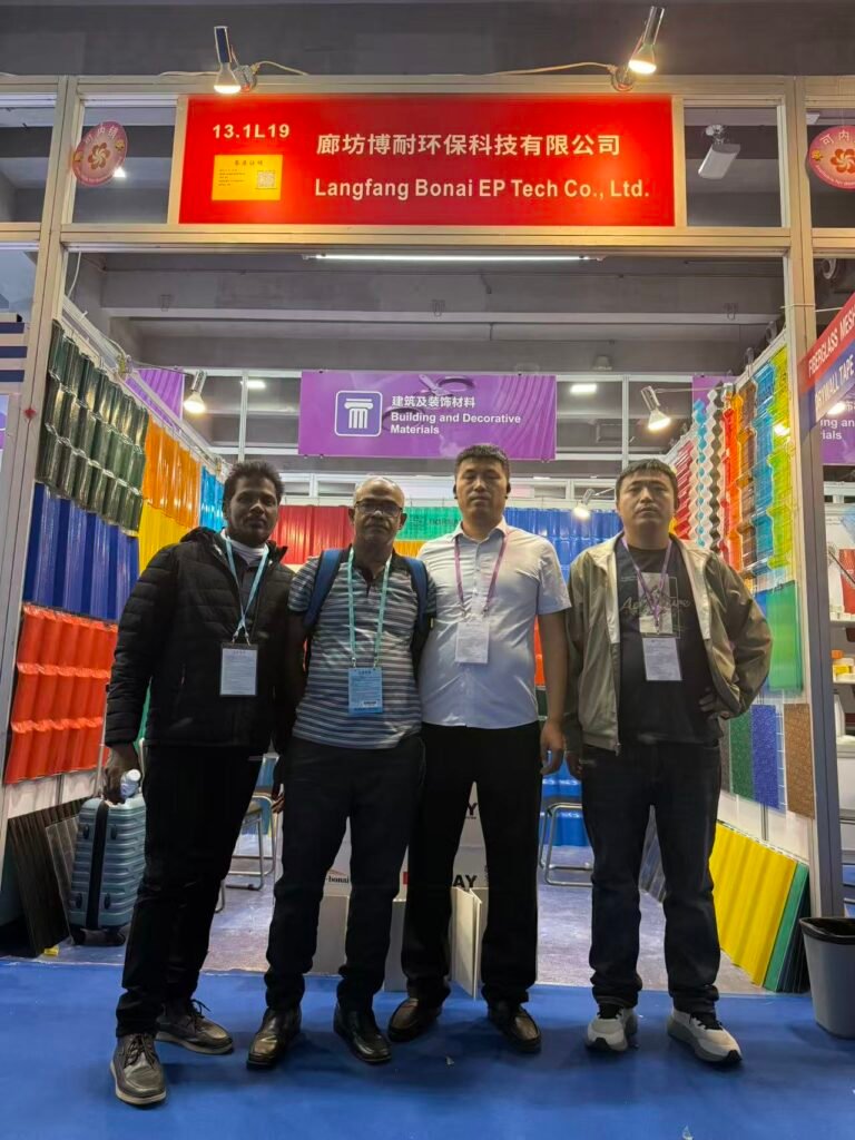 微信图片_20260330145643_459_14 - Four men with badges pose at a trade show booth for Langfang Bonai EP Tech Co., Ltd., in front of rainbow-colored building materials display side panels.