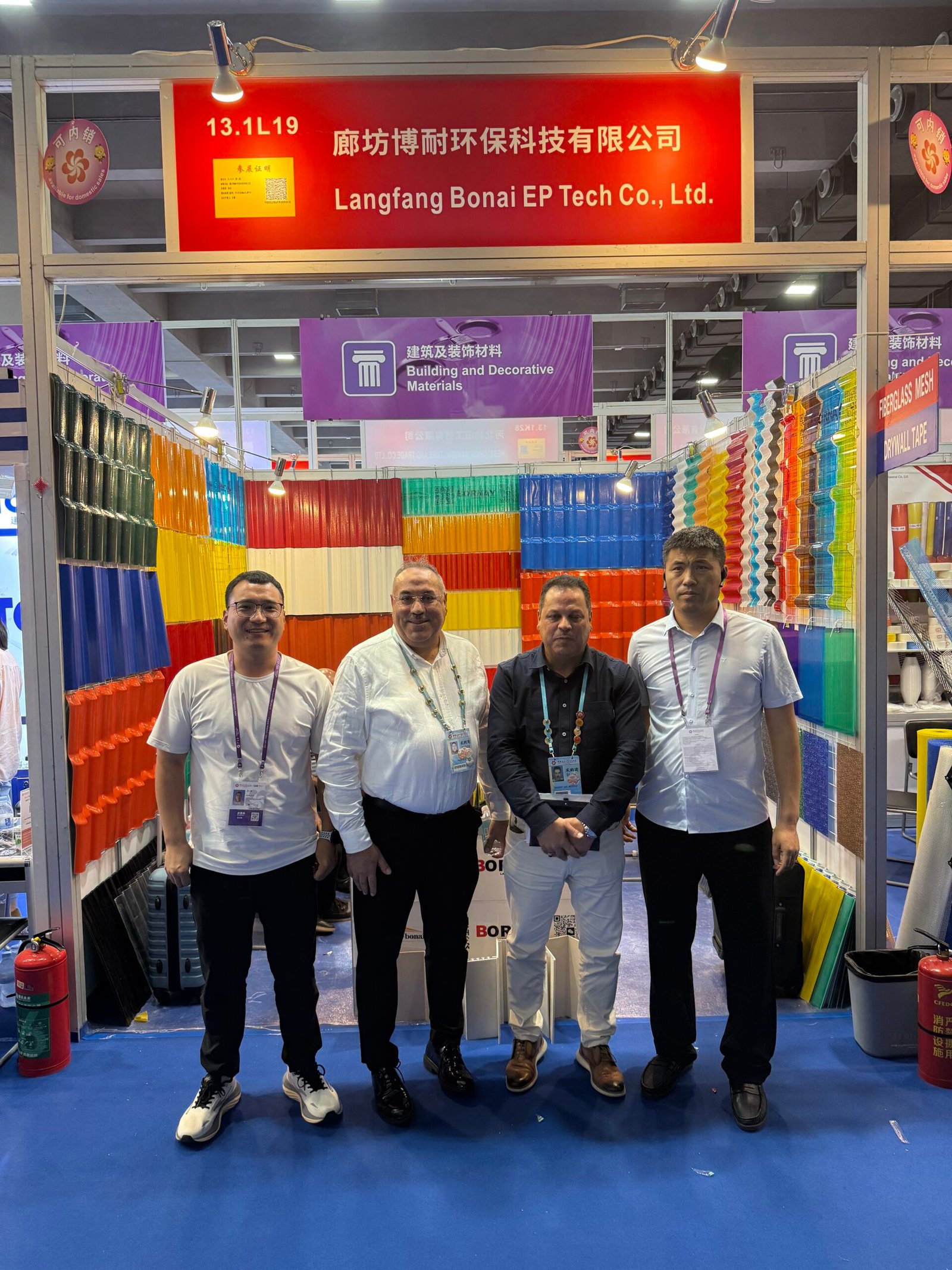 微信图片_20260330145649_461_14 - Four men pose at a trade show booth for Langfang Bonai EP Tech Co., Ltd, with rainbow-colored plastic sheets on display.