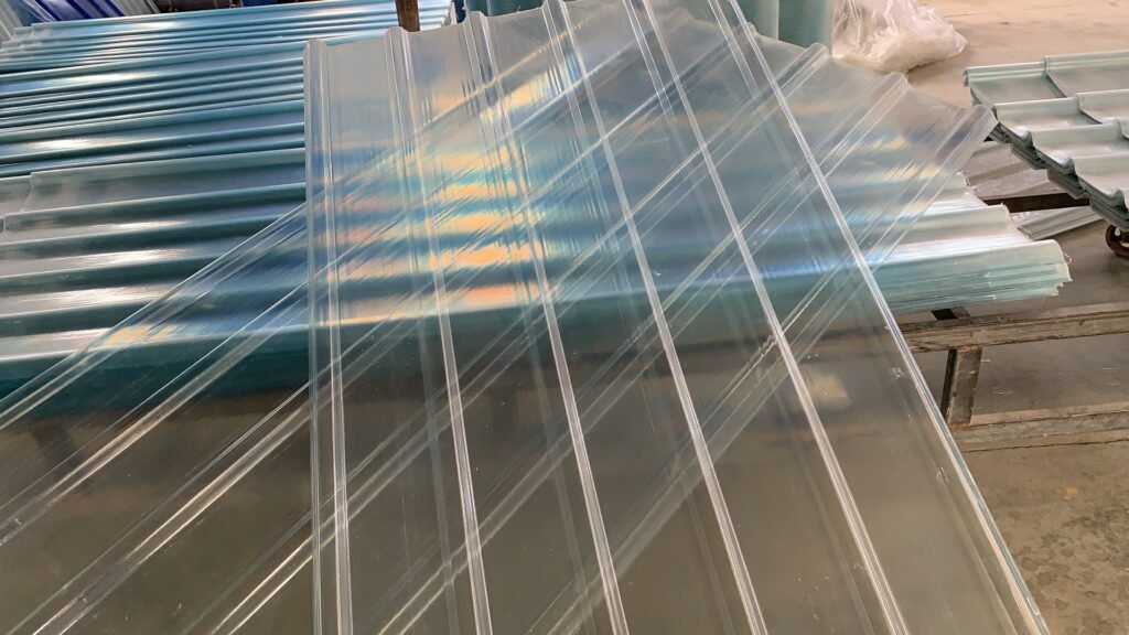 Clear corrugated plastic sheets stacked in a warehouse, reflecting light from above.