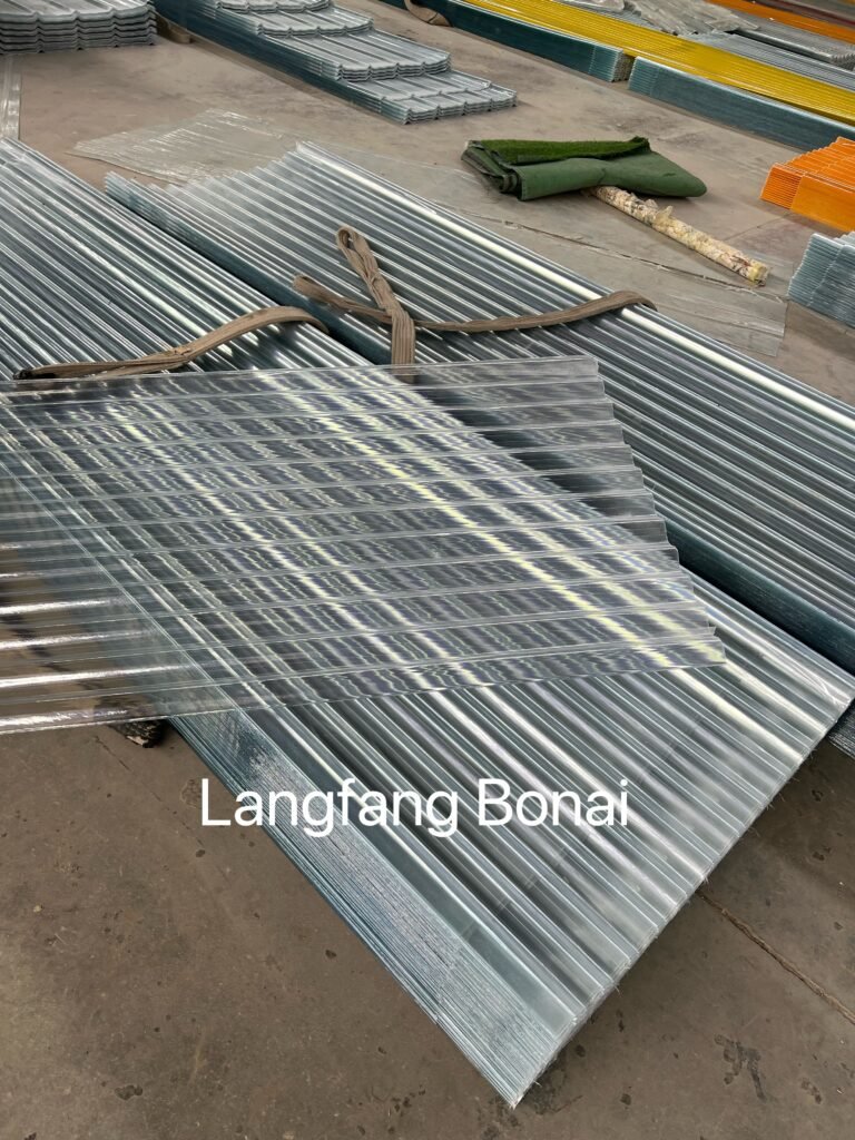 微信图片_20260416215253_752_4361 - Stacks of galvanized corrugated metal sheets tied with straps in a warehouse, with rolled green turf mats in the background.