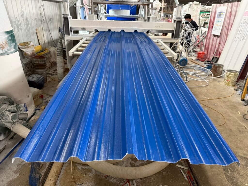 Blue corrugated metal sheet moves through a factory line, with a worker in a mask and tangled cables visible in the background.