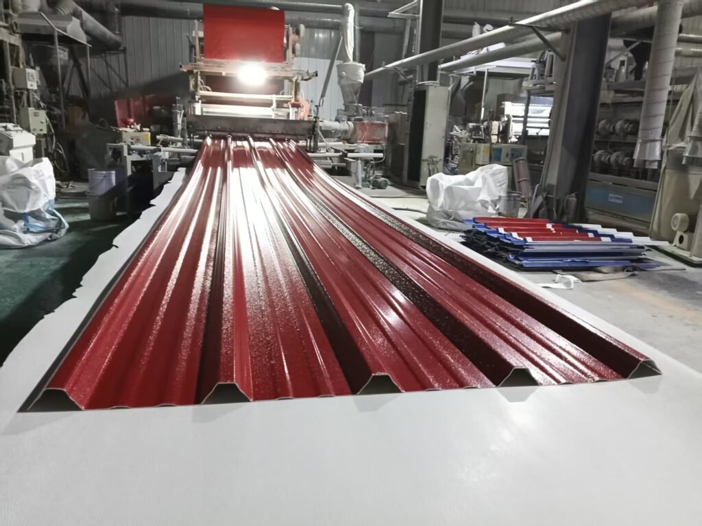 Red, glossy corrugated metal panels moving along an extrusion production line in a factory setting.