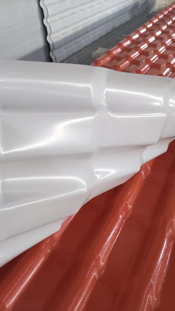 Close-up of a white molded plastic panel with curved grooves resting on a red metal surface in an industrial setting.