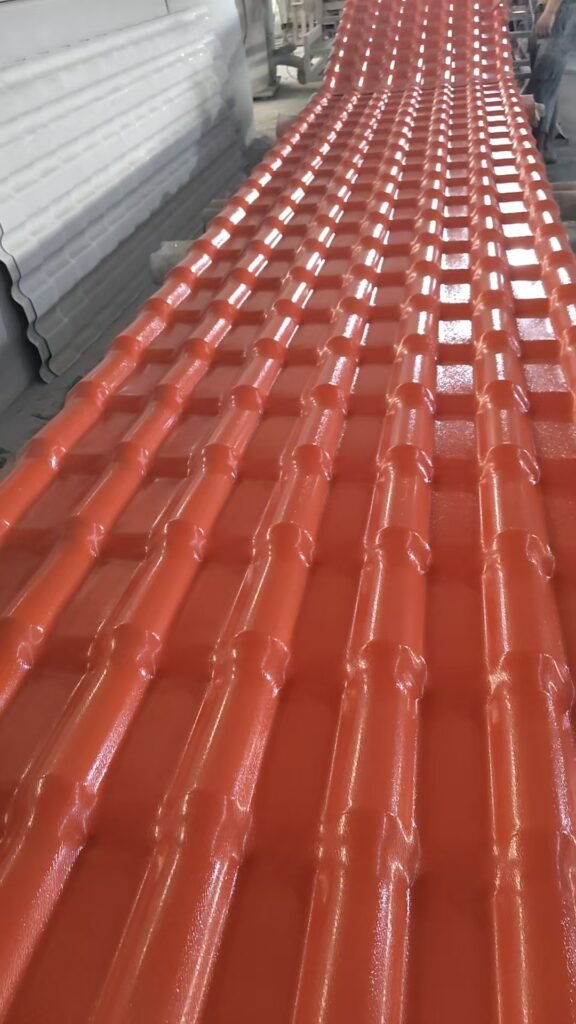 微信图片_20260806140504_4209_271 - Orange corrugated metal roofing sheets on a conveyor in a factory setting, ready for coating or drying.
