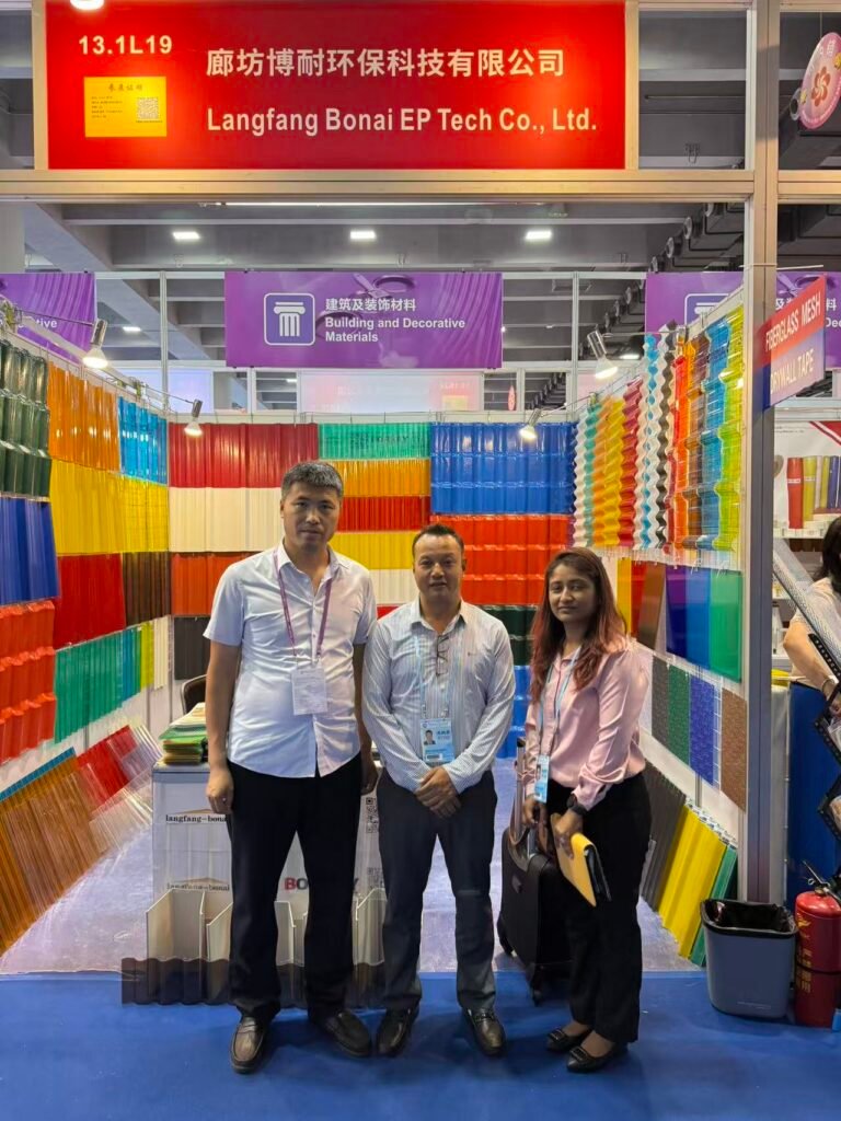 微信图片_20260330144023_420_14 - Three people stand in a colorful exhibition booth for Langfang Bonai EP Tech Co., Ltd., surrounded by lined display racks of bright plastic sheets in red, blue, yellow and other colors.