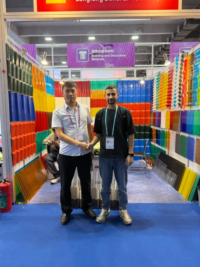 微信图片_20260330144044_430_14 - Two men shake hands in a booth surrounded by colorful wall samples under a purple 'Building and Decorative Materials' banner.